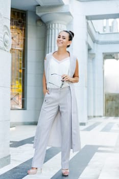 happy businesswoman in a pantsuit standing near a building