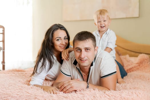 happy family lying on the bed and hugging, mom dad and little son