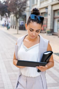 Confident young woman laughing and carrying notepad in hand while standing on the street, wearing stylish clothes