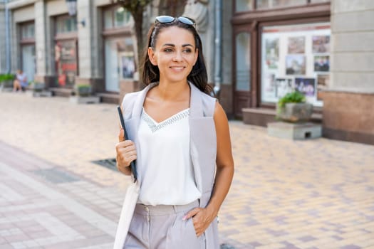 Beautiful woman smiling happy standing at city. Notepad in hand standing on street, in stylish clothes