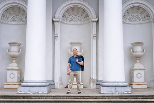 a man in casual clothes stands near the columns of a white building