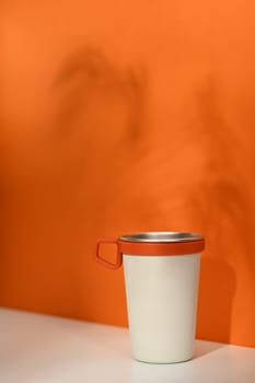 A stainless steel travel mug over orange background. Tumbler beverage container and Eco friendly lifestyle.