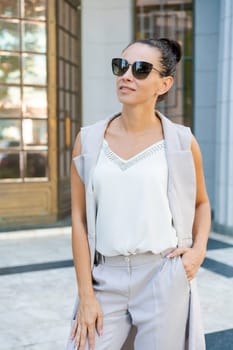 successful woman posing in a pantsuit and sunglasses on the steps of a building