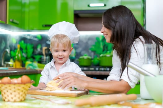 happy family mother and little son preparing dough in kitchen at table. products for dough are on table