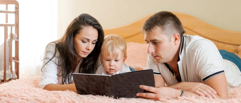 happy family lying on the bed reading a book, mom dad and little son banner
