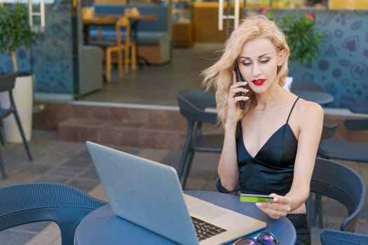 Beautiful woman in glasses sits at table in a street cafe and works on tablet with a laptop. The concept of remote work, free work schedule.