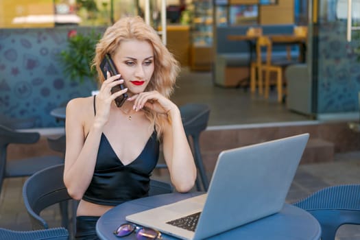 Beautiful woman in glasses sits at table in a street cafe and works on tablet with a laptop. The concept of remote work, free work schedule.