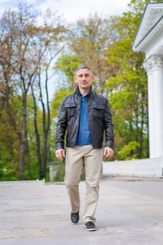 a man in casual clothes walks near a beautiful building and looks at the camera