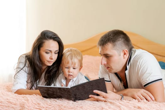 happy family lying on the bed reading a book, mom dad and little son