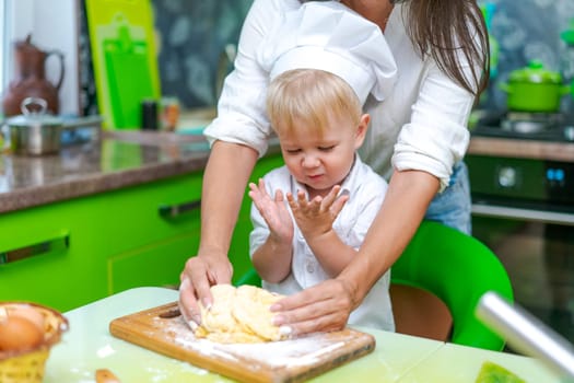 happy family mother and little son preparing dough in kitchen at table. products for dough are on table