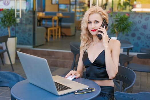 Beautiful woman in glasses sits at table in a street cafe and works on tablet with a laptop. The concept of remote work, free work schedule.