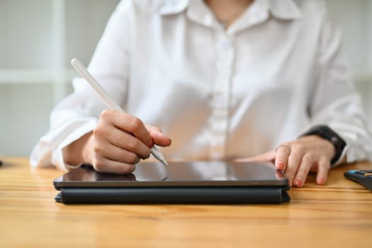 Unrecognizable young creative woman using stylus pen writing notes or drawing on digital tablet.