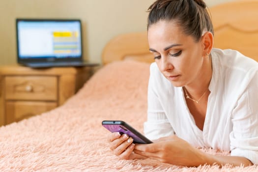 cute woman lying on the bed with a phone in her hand on a soft pink blanket