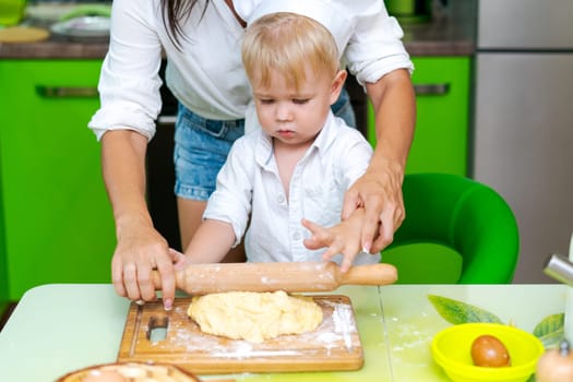 happy little boy preparing dough in kitchen at table. there are dough products on table, dressed as chef