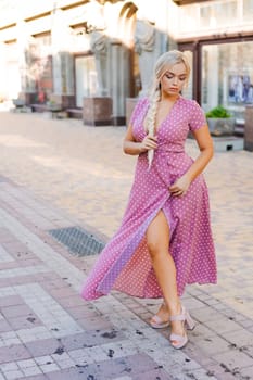 beautiful woman with long braid in pink dress with white polka dots posing on street in the city