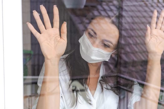 woman with a protective mask looks out the window with longing