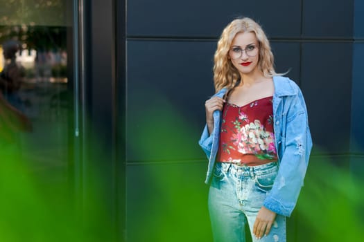 beautiful blonde woman wearing glasses and wearing blue denim and jeans posing on street in city