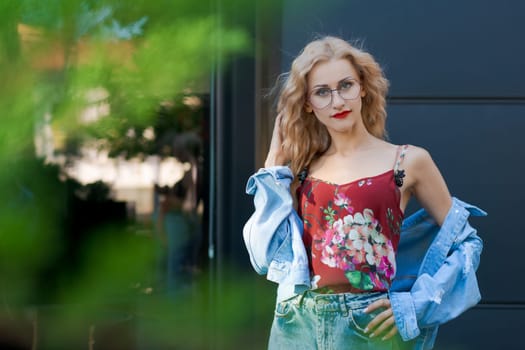 beautiful blonde woman wearing glasses and wearing blue denim and jeans posing on street in city