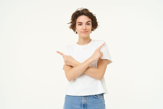 Puzzled woman makes choice, points fingers left and right, deciding, confused what to pick, stands over white studio background.