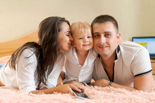 happy family lying on the bed and hugging, mom dad and little son