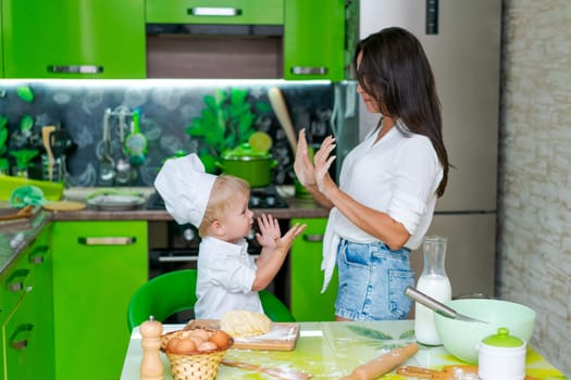 happy family mother and little son preparing dough in kitchen at table. products for dough are on table