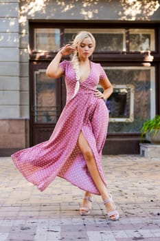beautiful woman with long braid in pink dress with white polka dots posing on street in the city
