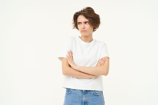 Portrait of offended girl, student pouting, cross arms on chest and looking away, standing disappointed against white studio background.