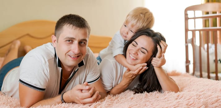 happy family lying on the bed and hugging, mom dad and little son