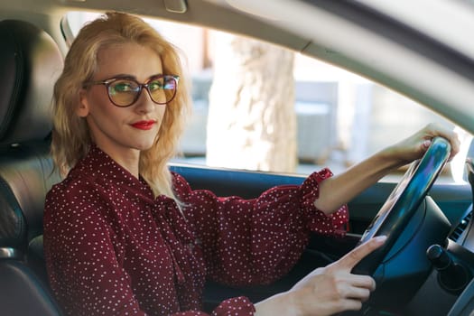 beautiful successful blonde woman in a red dress sitting in a car behind the wheel