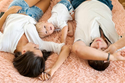 happy family lying on the bed , mom dad and little son