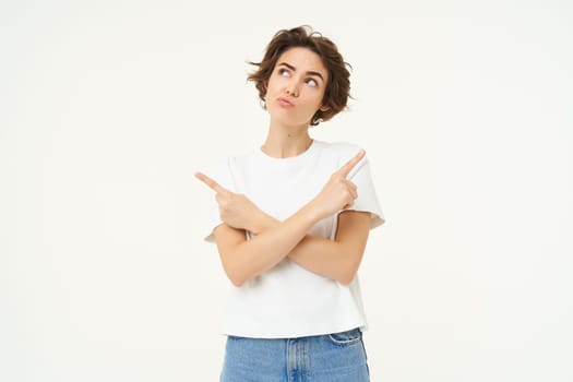 Portrait of brunette woman with thoughtful face, pointing sideways, making choice, decision, standing over white studio background.