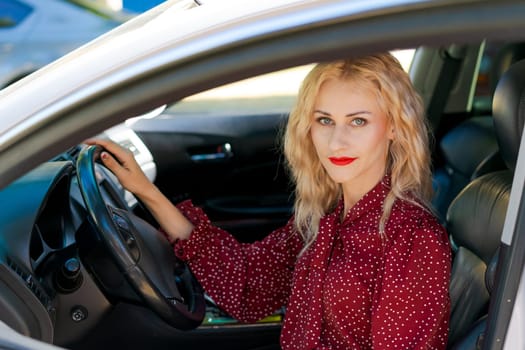 beautiful successful blonde woman in a red dress sitting in a car behind the wheel