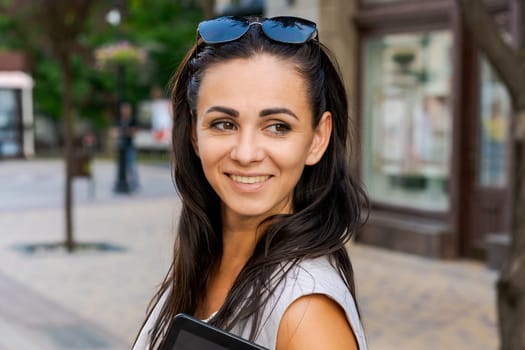 Confident young woman laughing and carrying notepad in hand while standing on the street, wearing stylish clothes