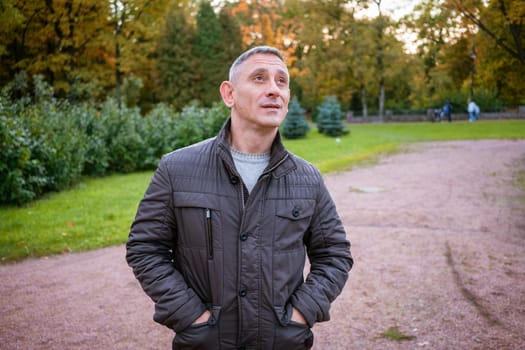 a man in an autumn jacket in the park stands on the path