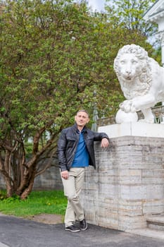 a man in casual clothes stands near a beautiful white building with lions