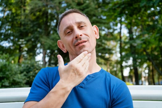 handsome portrait of a man in a blue T-shirt sitting on a park bench