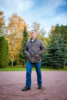 a man in an autumn jacket in the park stands on the path