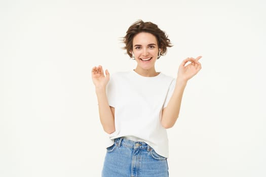 Portrait of happy smiling woman in wireless earphones, dancing and listening to music, enjoying her favourite song, posing over white background.