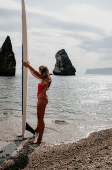 Close up shot of beautiful young caucasian woman with black hair and freckles looking at camera and smiling. Cute woman portrait in a pink bikini posing on a volcanic rock high above the sea