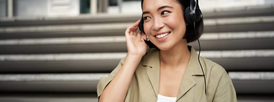 Portrait of beautiful girl in earphones, listening music, smiling and walking in city centre.