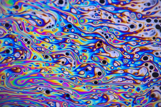 Bright green, pink, purple, blue and orange pastel colours swirl around intense black and white dots patterns on the surface of a soap bubble.