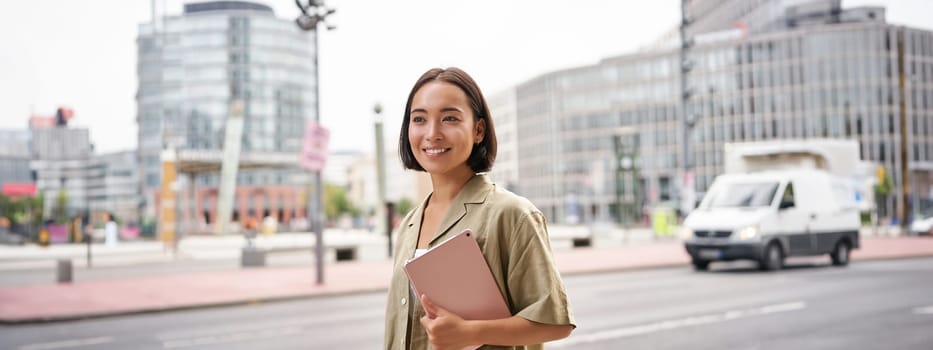 Portrait of young stylish woman walking with tablet, going somewhere in city.