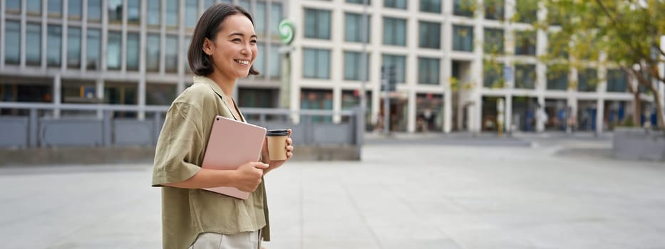 Stylish city girl with tablet, walking on street and drinking takeaway coffee, going to university or work.