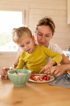 rested Caucasian mother hugs her baby boy while sitting in the kitchen.