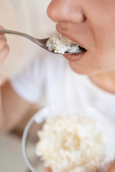 woman puts a spoon of rice in her mouth.