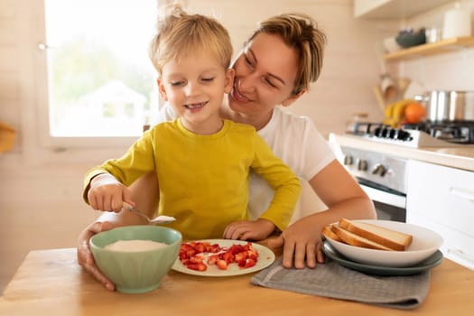 lifestyle concept, young mother and son sitting at the table in the kitchen with plates of food.