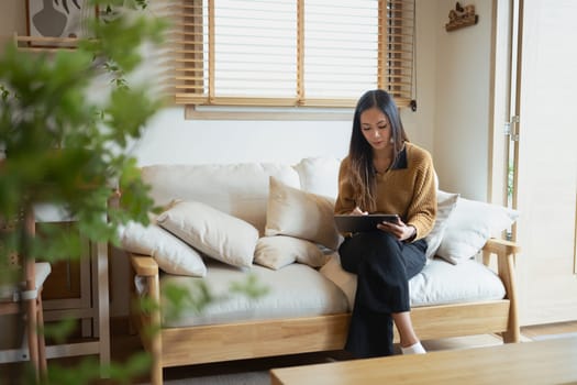 Peaceful millennial woman working with digital tablet in a minimalist living room.