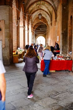 Cremona, Lombardy, Italy - November 7th 2024 Shoppers browse stalls selling various goods in a historic market hall with brick arches and festive lighting