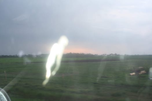 A rural setting showcases an overcast sky and a hint of twilight glow on the horizon. Blurred details from a passing vehicle create a sense of motion and atmosphere during the early evening.
