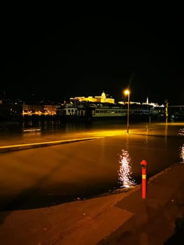 A waterfront area is submerged in water during the night, reflecting city lights and the skyline, creating a serene yet dramatic atmosphere.